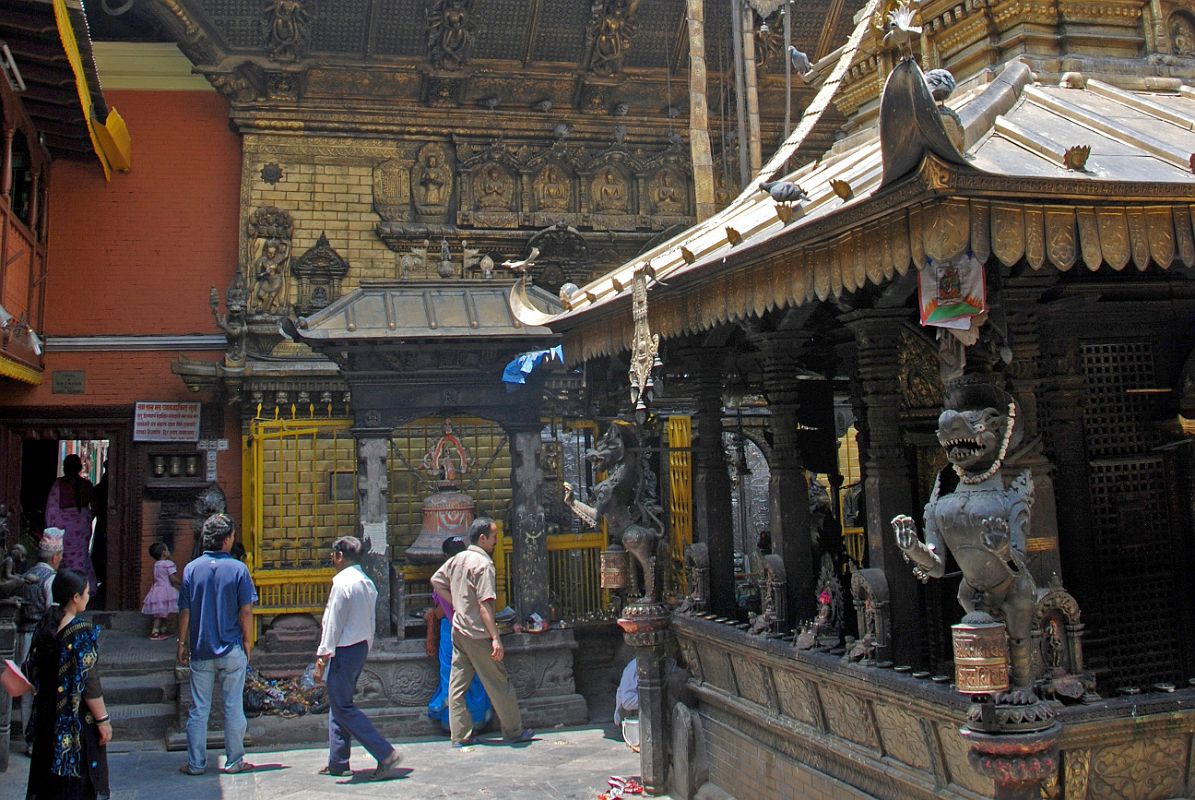 Kathmandu Patan Golden Temple 11 Swayambhu Chaitya Left Side On the four corners of the Swayambhu Chaitya at the Golden Temple in Patan are mystical lions with long pointed teeth, sharp curled claws, long curving snouts, standing on the hind legs. To the left is the main Golden Temple with the five Dhyani Buddhas carved on the wall, and wood-carvings of many-armed deities on the roof struts.